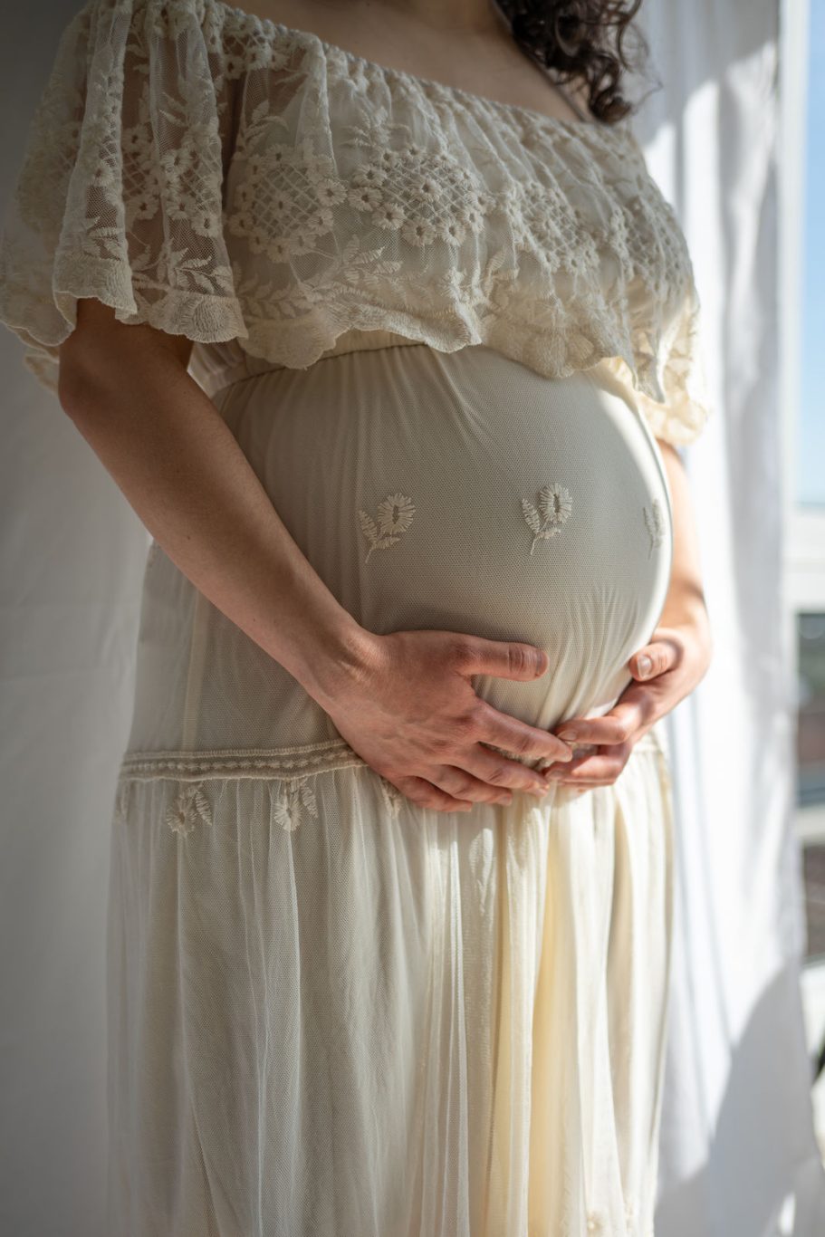 Schwangere Frau in einem weißen Kleid, die ihren Bauch sanft hält.