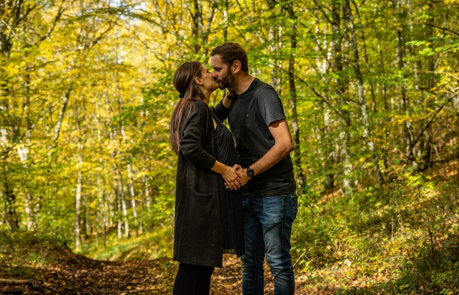 Ein Paar küsst sich in einem herbstlichen Wald mit bunten Blättern.