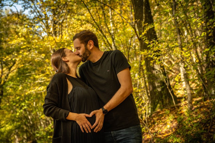 Schwangere Frau und Mann umarmen sich in einem Wald mit herbstlichen Farben.