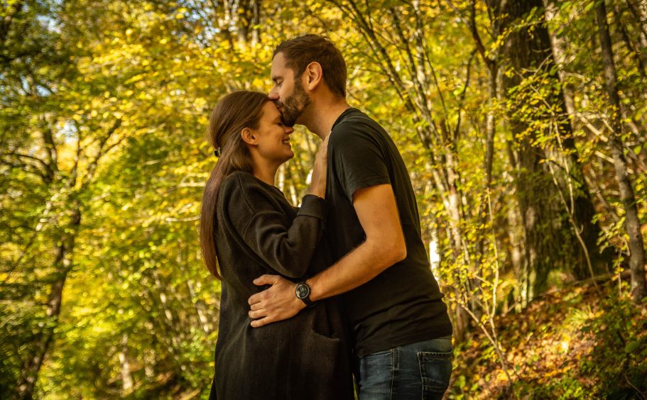 Paar umarmen sich in einem herbstlichen Wald mit buntem Laub im Hintergrund.