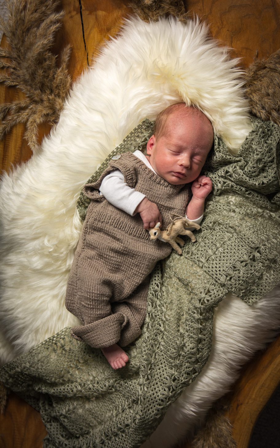 Neugeborenes Baby in einem beigen Strampler, auf einer weichen Decke liegend.